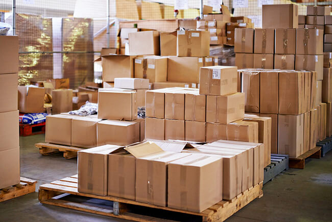 Boxes on pallets in a messy warehouse, representing a retailer's disorganised fulfilment process before outsourcing to a 3PL