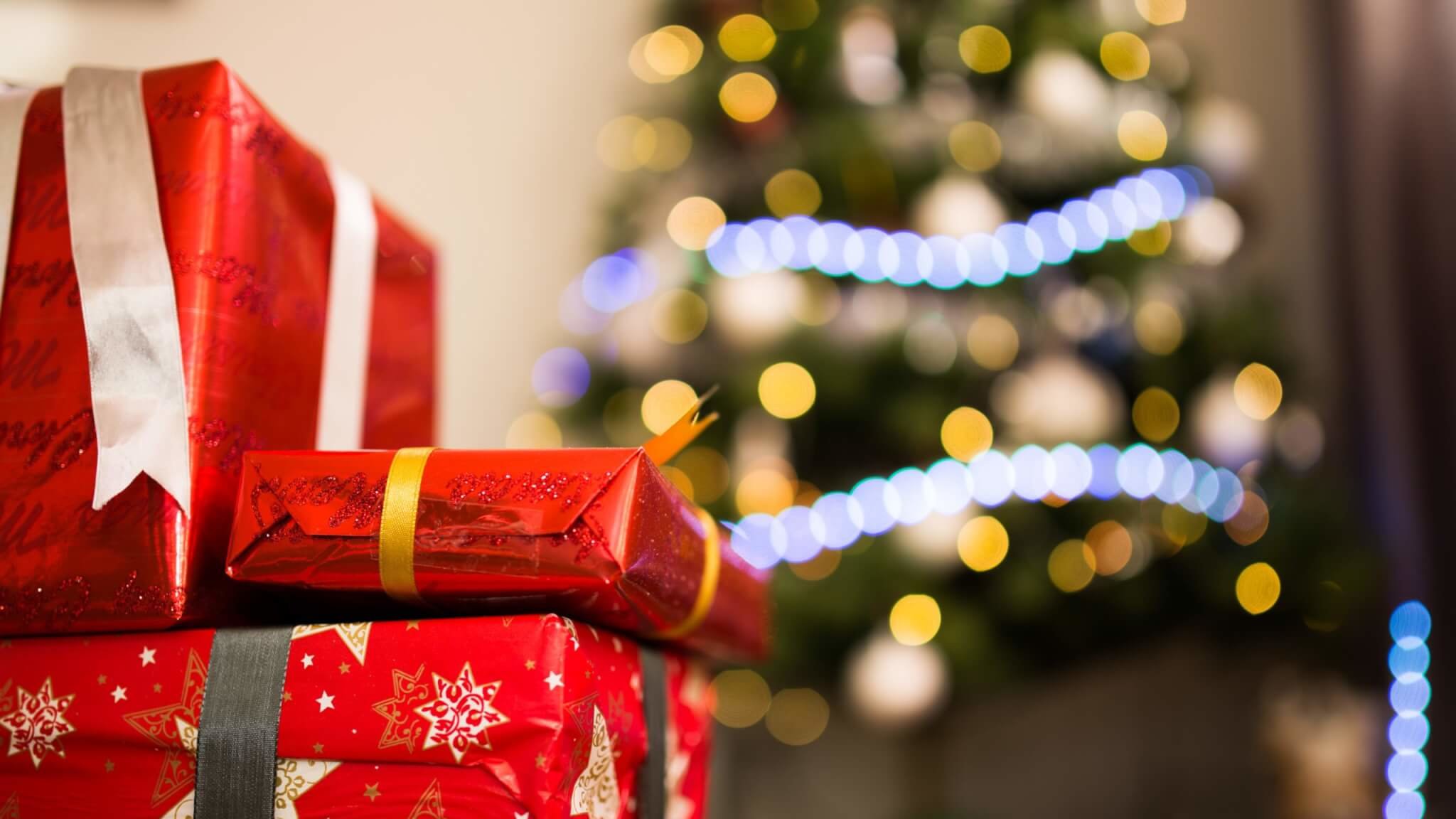 A selection of Christmas gifts in front of a lit Christmas tree